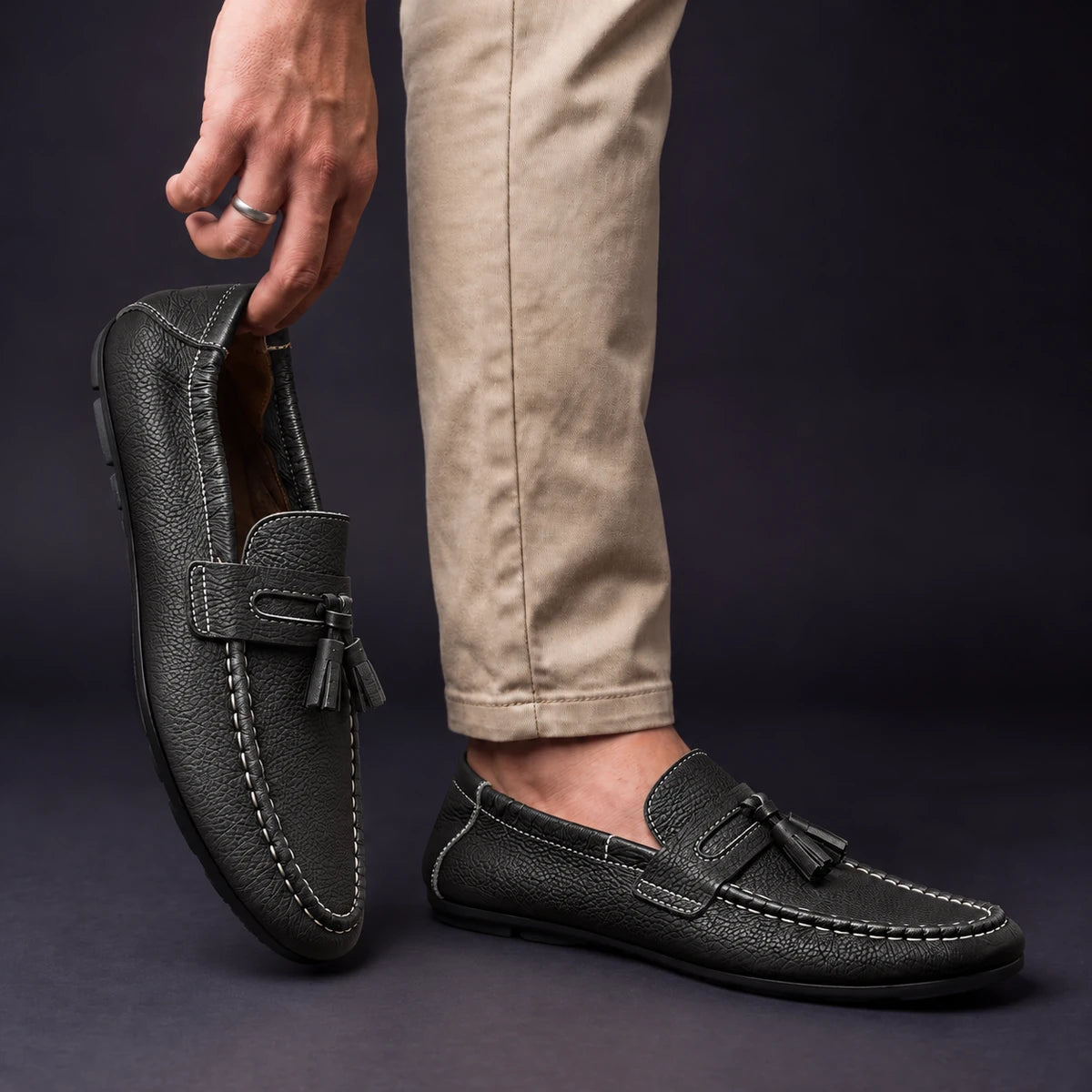 Cowhide Leather Loafers | Viggo Black model holding shoe by heel opening beside matching worn shoe